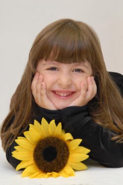 Little girl smiling and laying on the floor with sunflower in portrait studio
