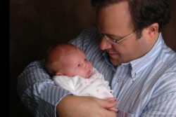 father holding newborn daughter in arms with black background