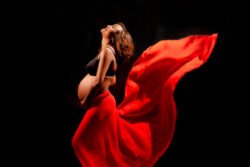 dramatic artistic maternity portrait of a pregnant woman wrapped in flowy red sheet with black background